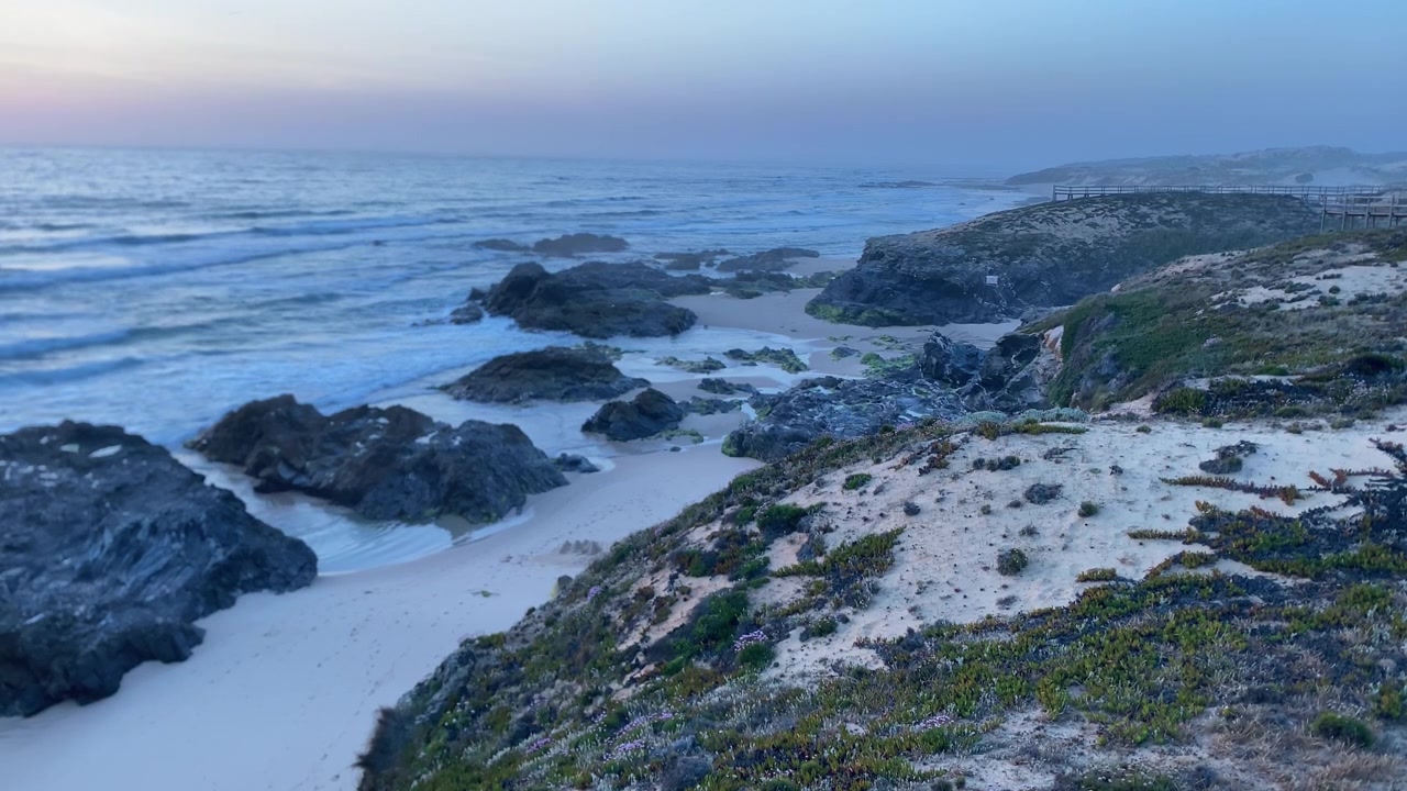 Alentejo Portugal rugged coast with crashing waves on a sandy beach and rock formations during the tranquil twilight hour