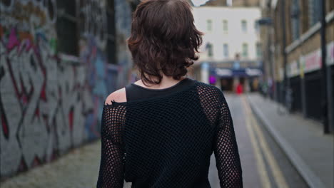 outdoor fashion portrait of young alternative style woman turning around and smiling walking along graffiti covered walls of london city street uk in real time