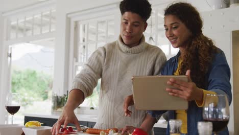 Video-of-happy-biracial-couple-preparing-meal-together-and-using-tablet