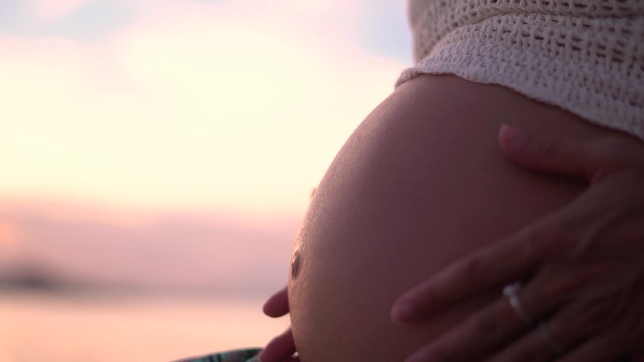 Gravid mage, vordende mor slapper av på stranden ved solnedgang.