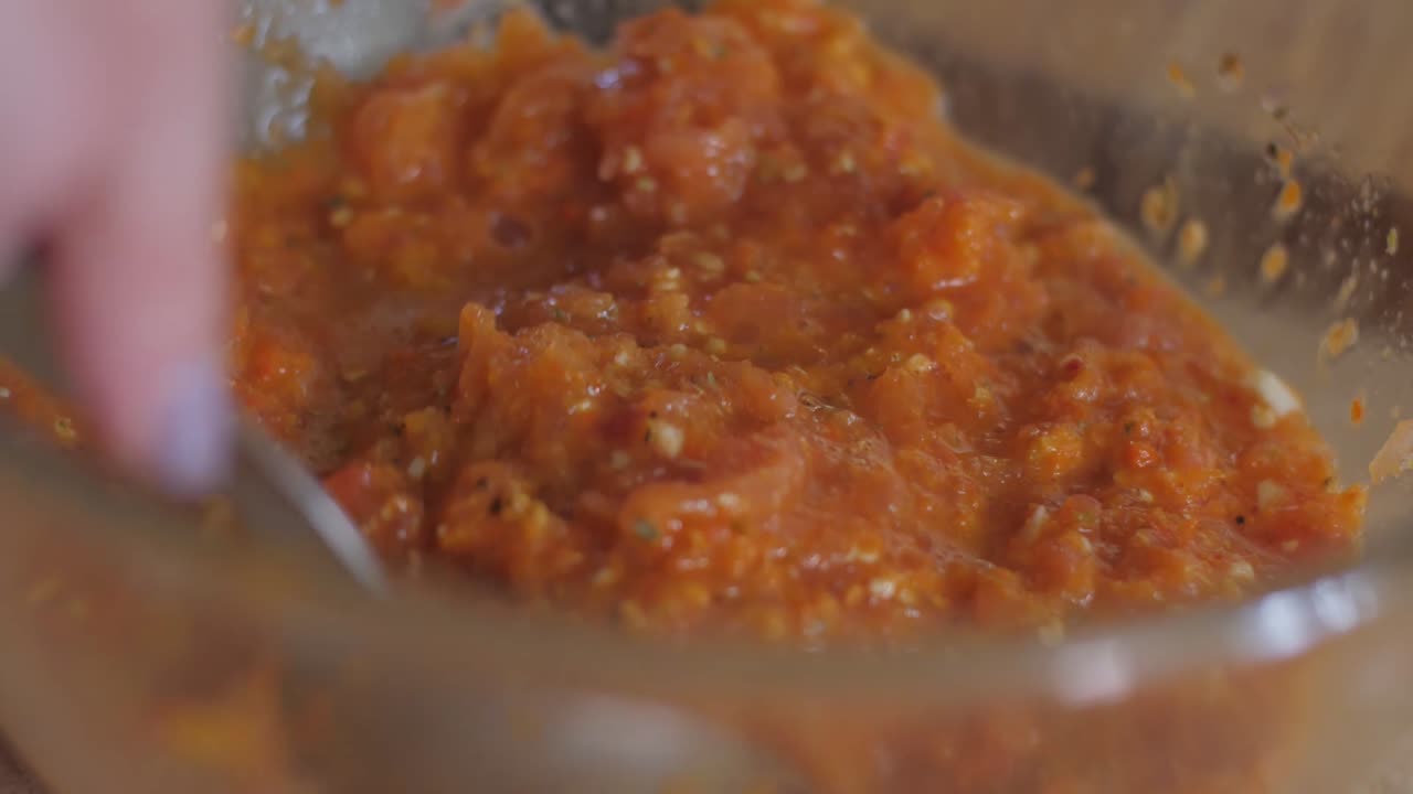 Mixing fresh tomato and herb sauce in a glass bowl