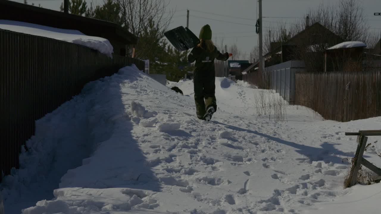 Persona che cammina nella neve alta portando una pala in una giornata invernale di sole