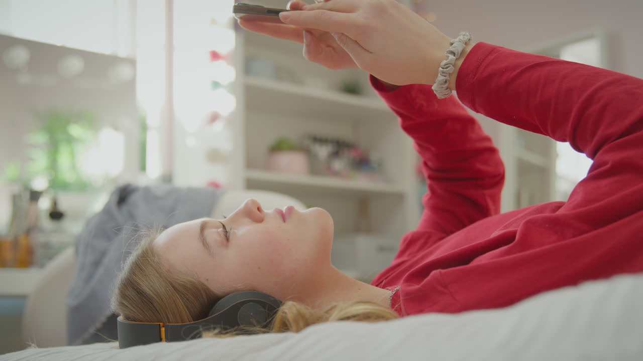 무선 헤드폰을 착용 한 십대 소녀가 휴대전화에서 음악이나 영화를 스트리밍 - 느린 동작으로 뜨겁다