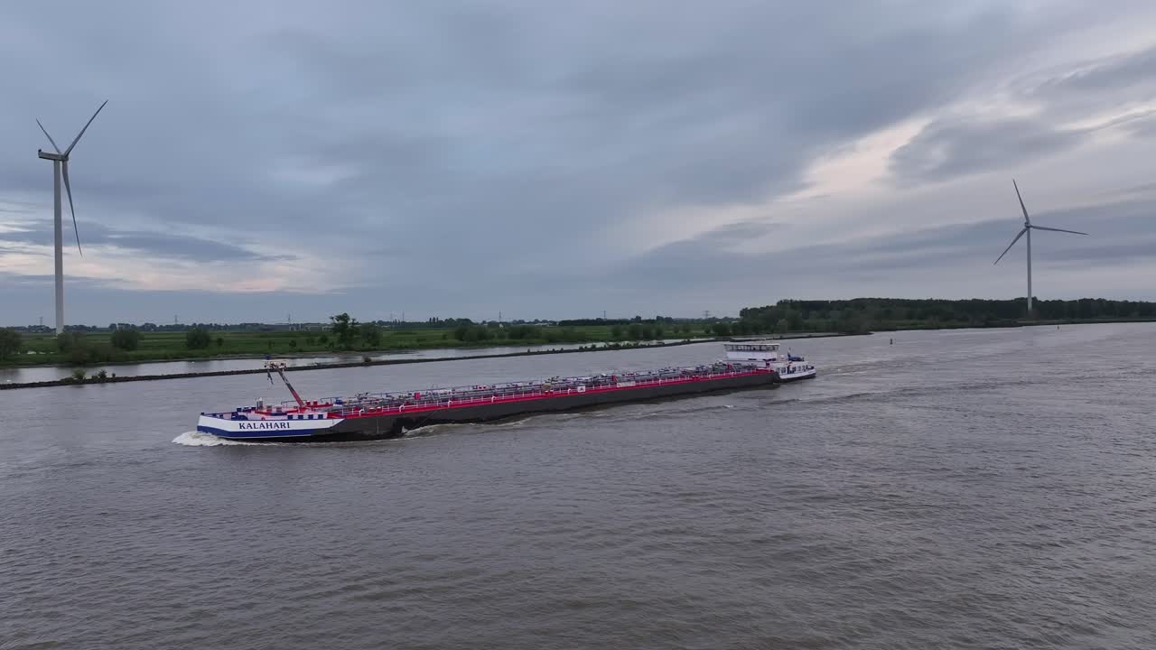 Cargo ship sailing on a river with wind turbines in the background at dusk