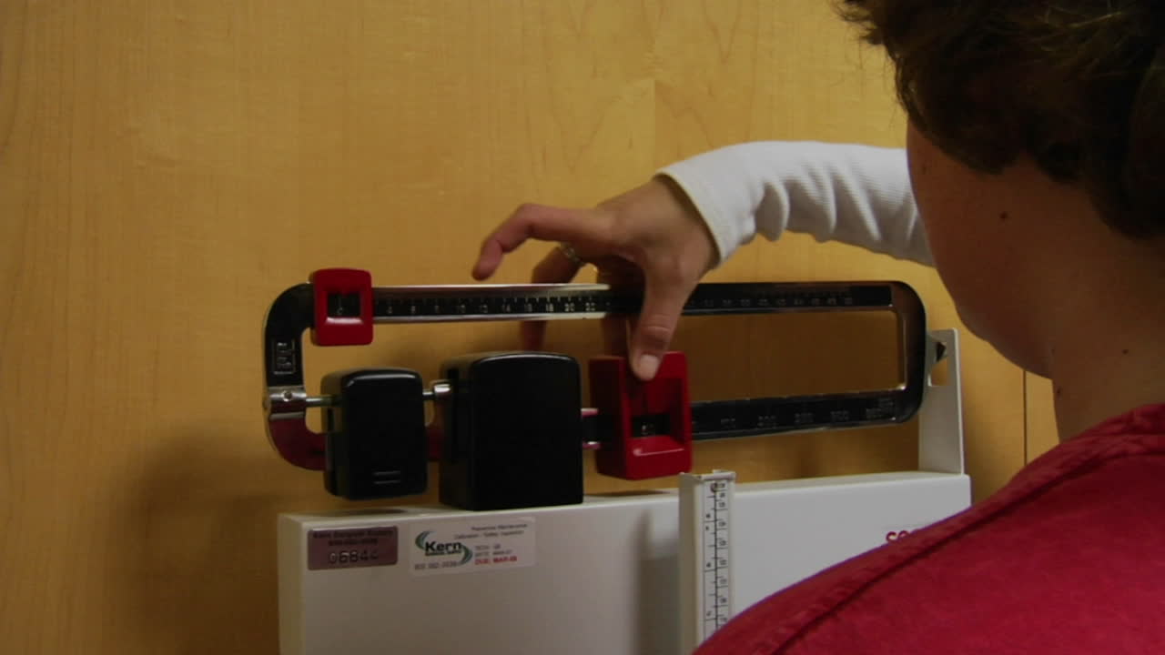 una enfermera pesa a un paciente en una báscula de consultorio médico