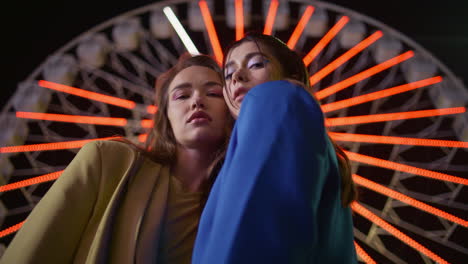 two girls posing ferris wheel at night closeup. gorgeous friends in luna park