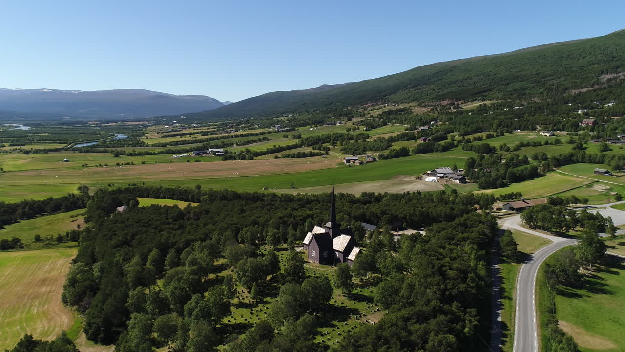 fotografía aérea de una iglesia de madera con un cementerio, situada entre campos verdes y paisajes rurales.