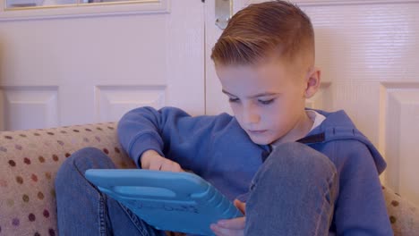 Close-up-of-a-child-playing-games-on-a-tablet-while-sitting-on-a-sofa-at-home