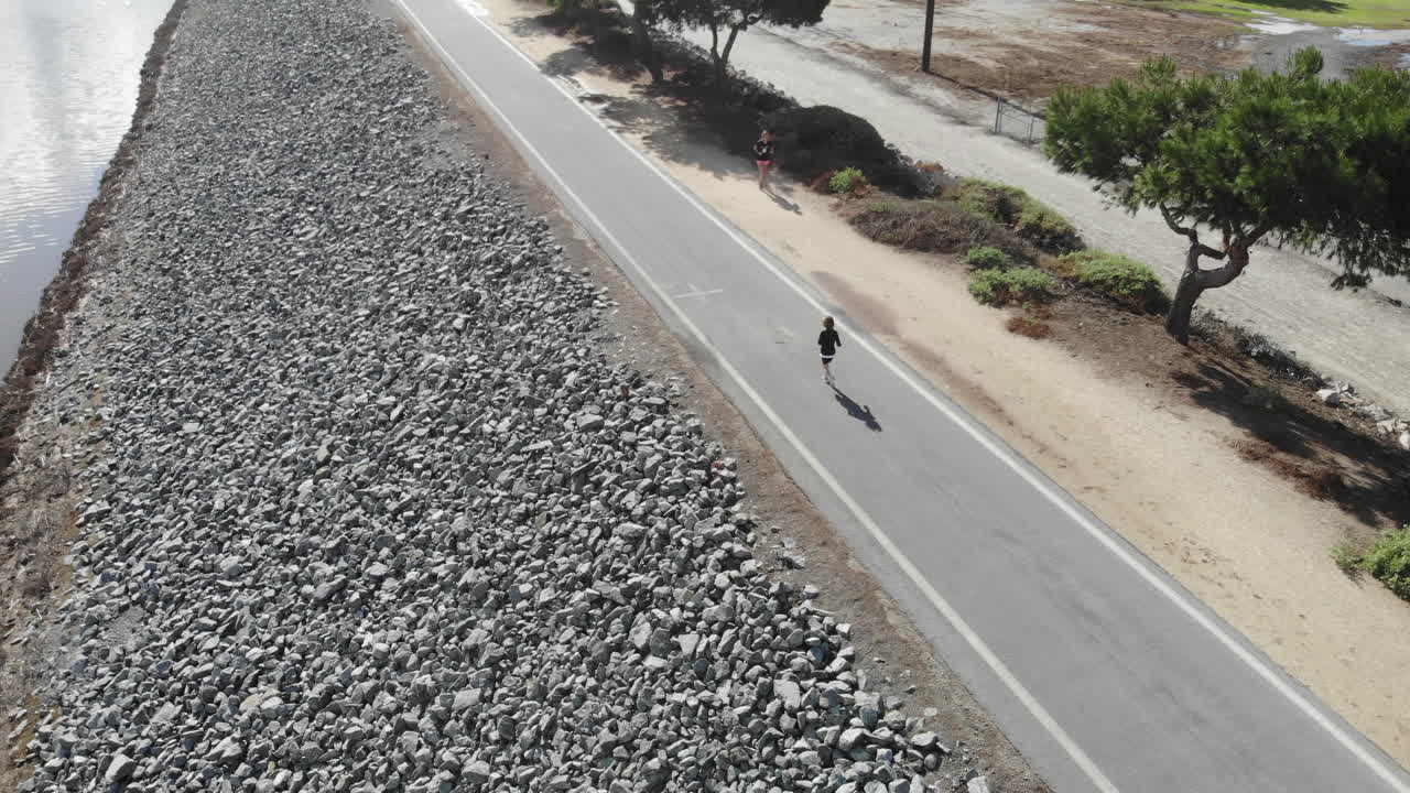 A 4K rotating aerial drone of a young boy as he runs along the riverbed for his daily workout.