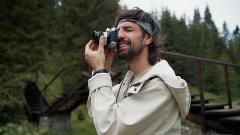 Portrait-of-a-tourist-brunette-guy-who-photographs-a-view-of-the-green-forest.-Guy-in-a-white-jacket-on-a-hike