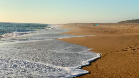 Waves-crashing-onto-the-shore-during-sunset-in-Nazare,-Portugal