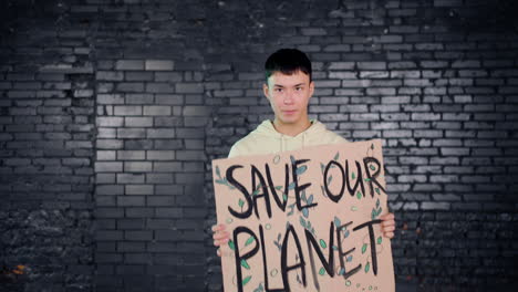 asian young environmental activist holding a cardboard with save the planet" inscription and protesting while looking at the camera"