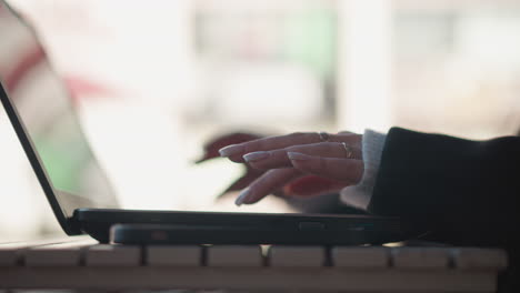 close-up of hands typing on laptop keyboard adorned with polished nails and delicate rings, hand reflection visible on the screen, showcasing a modern remote worker