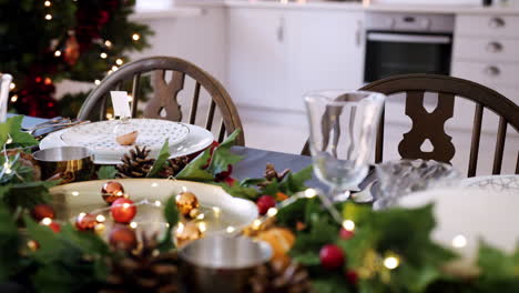 Mid-section-of-a-woman-laying-cutlery-at-a-place-setting-on-a-dining-table-decorated-for-Christmas-dinner,-selective-focus