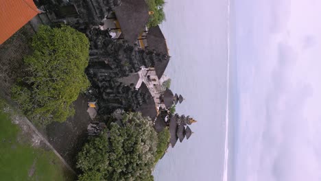 vertical drone video of a giant historical hindu temple at bali next to the sea