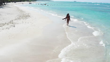Aerial---Caribbean-holiday-vibes,-female-beachgoer-strolls-on-white-sand-beach-near-Puerto-Plata,-Dominican-Republic