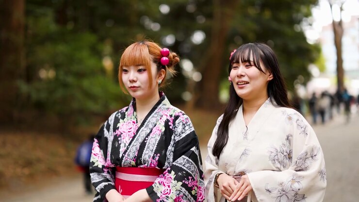 Due donne sorridenti in kimono tradizionale passeggiano nel parco alberato del Santuario Meiji, Tokyo