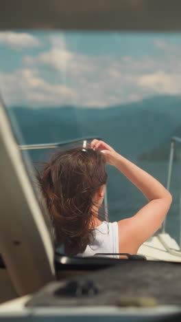 modern yacht with lady on deck sails to large mountains on summer day. woman with waving hair rides motorboat on weekend. happy time at seaside