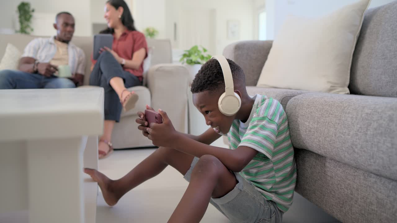 Diverse family watching son playing phone at home, winning game, standing, cheering, copy space