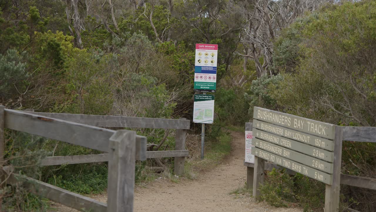 Camera slowly pans past wooden fence and trailhead signs at bushland walking track entrance