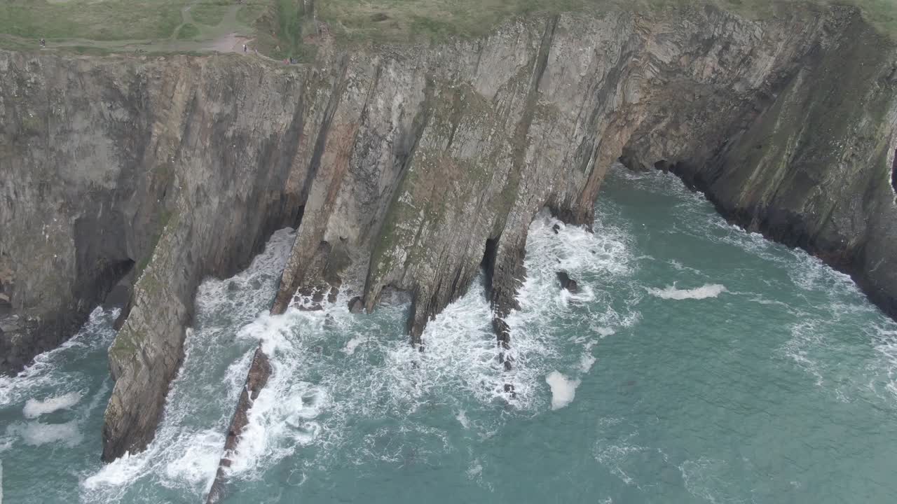 Stationary aerial view of sea side cliffs with rough seas and waves hitting the cliffs
