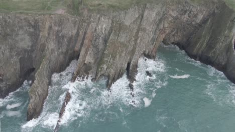 stationary aerial view of sea side cliffs with rough seas and waves hitting the cliffs
