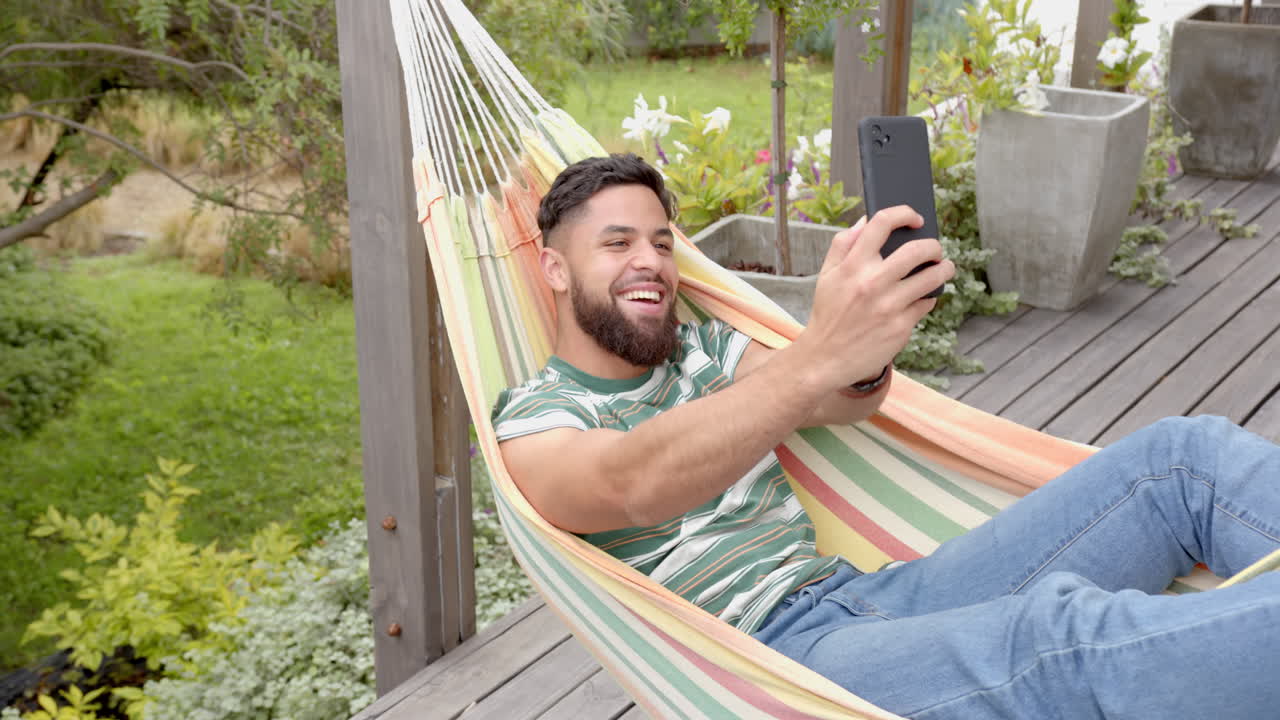 Relaxing in hammock, man taking selfie with smartphone in backyard garden