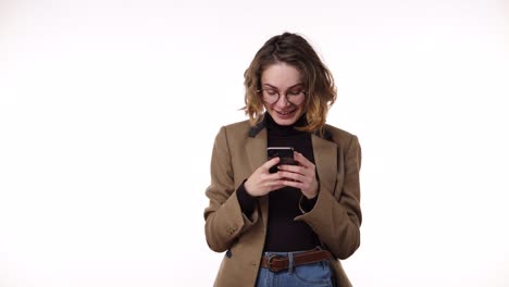 portrait of happy european woman wearing casual clothing - brown jacket and jeans, holding smartphone and typing text message or