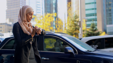 Vista-Lateral-De-Una-Joven-Asiática-Con-Hijab-Usando-Un-Reloj-Inteligente-En-La-Ciudad-4k