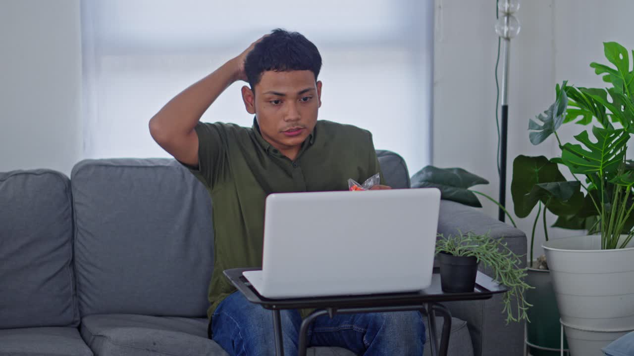 Young man surprised by sudden ceiling leak while using his laptop at home