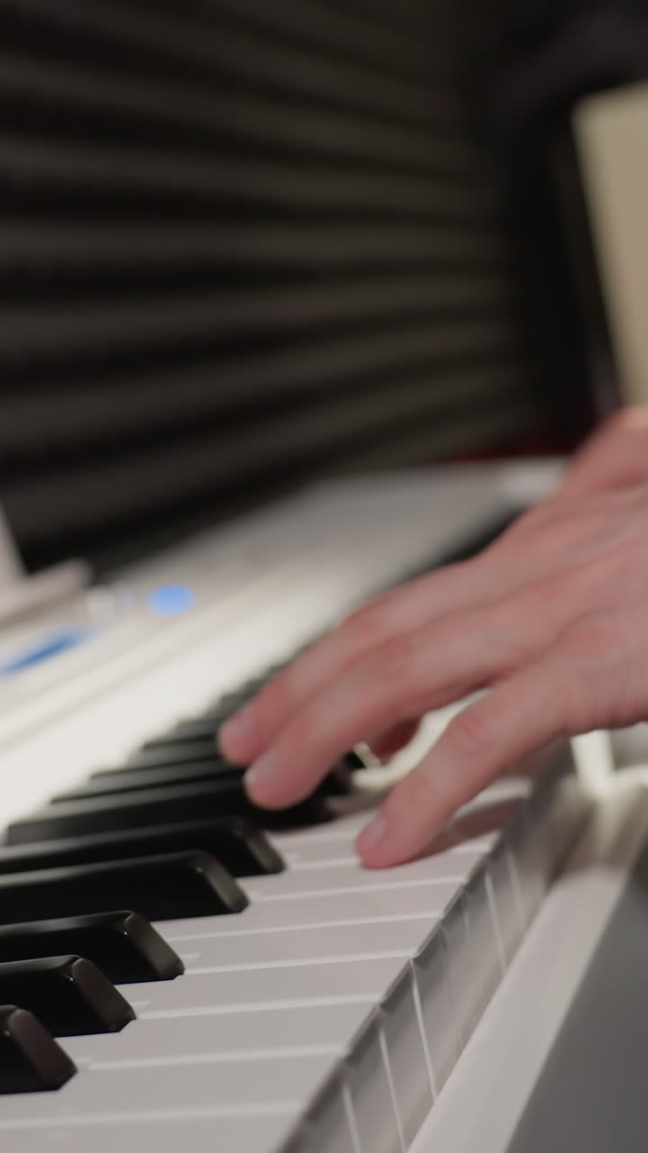 vista lateral de la mano de un músico con una camisa de manga larga azul tocando un piano blanco, con una pared acústica negra en el fondo. el enfoque está en las teclas del piano y la mano