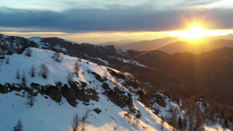 Snow-covered-mountain-wilderness-terrain-glows-in-golden-sunset,-aerial-trucking