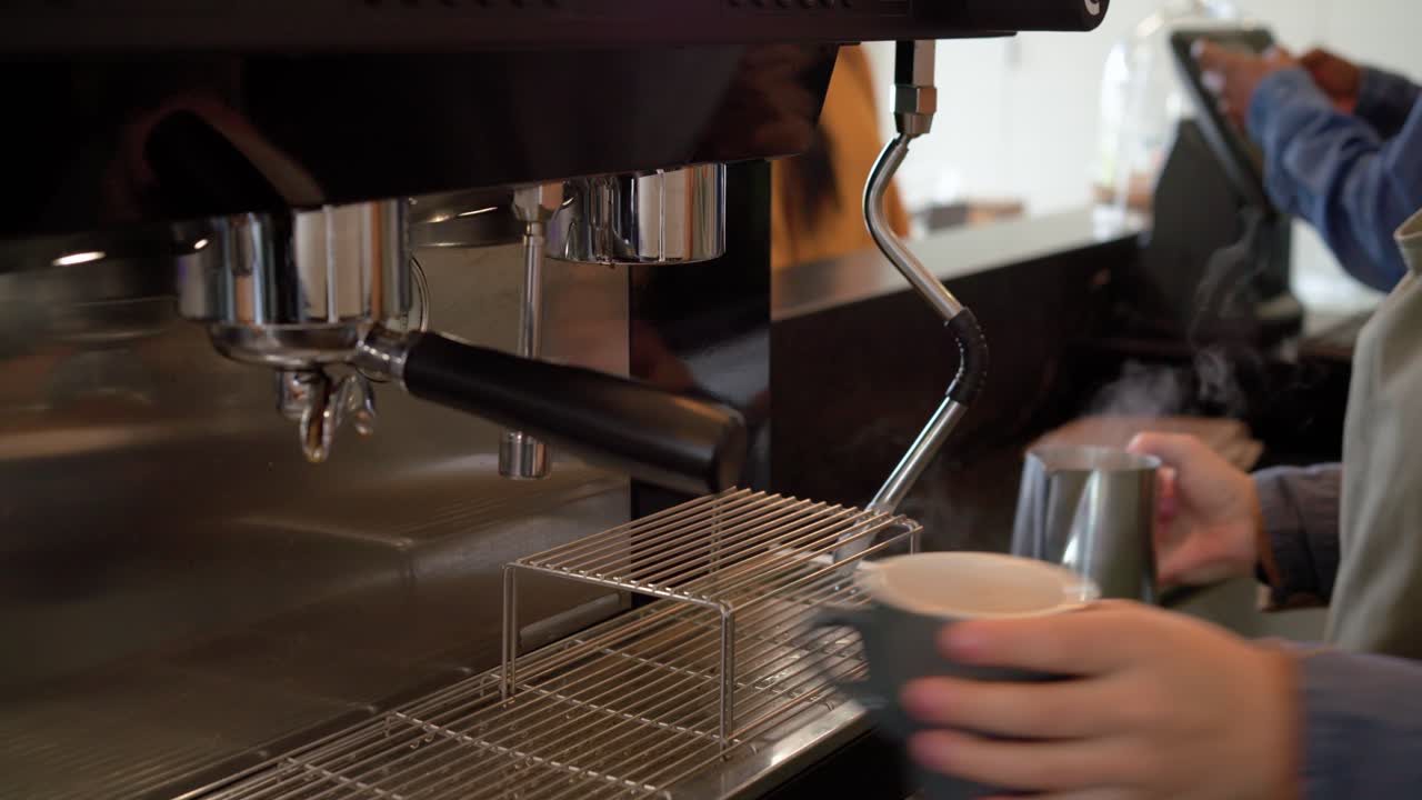 Manopola del vapore che gira, barista che monta il latte in un bricco di acciaio inossidabile sul bancone per la schiuma dell'espresso