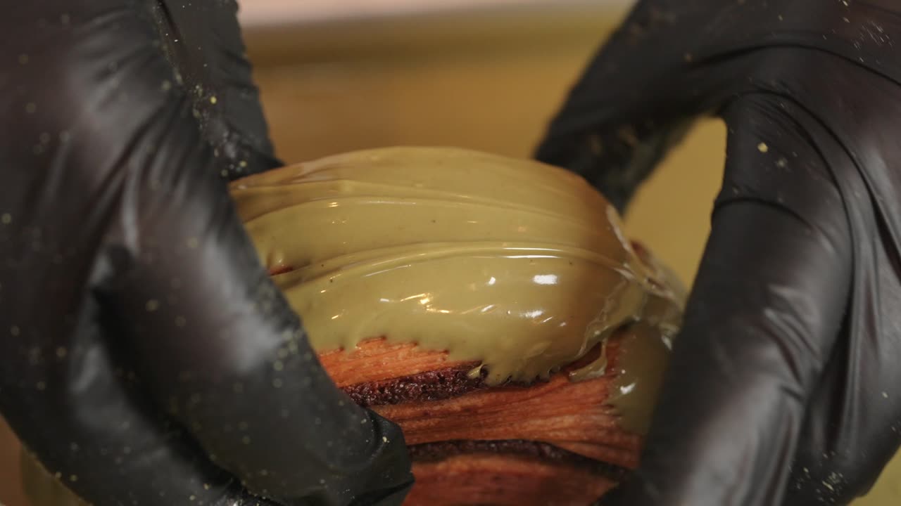 Pistasjcroissant-donut som pyntes ved å rulles i krem, sett ovenfra.