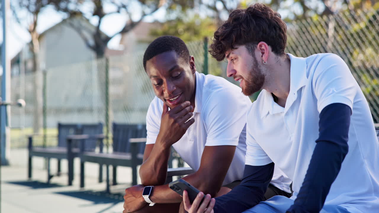 Two Young Men Relaxing and Talking on a Tennis Court with a Smartphone