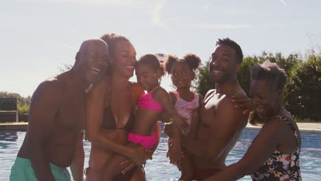 Portrait-Of-Smiling-Multi-Generation-Family-On-Summer-Holiday-Relaxing-In-Swimming-Pool