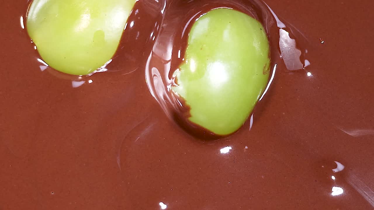 Close-up of green grapes partially covered in glossy, flowing chocolate, highlighting the rich texture and contrast.