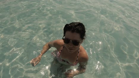 A-beautiful-girl-in-her-20s-in-swimwear-and-sunglasses-waving-at-the-camera-and-smiling