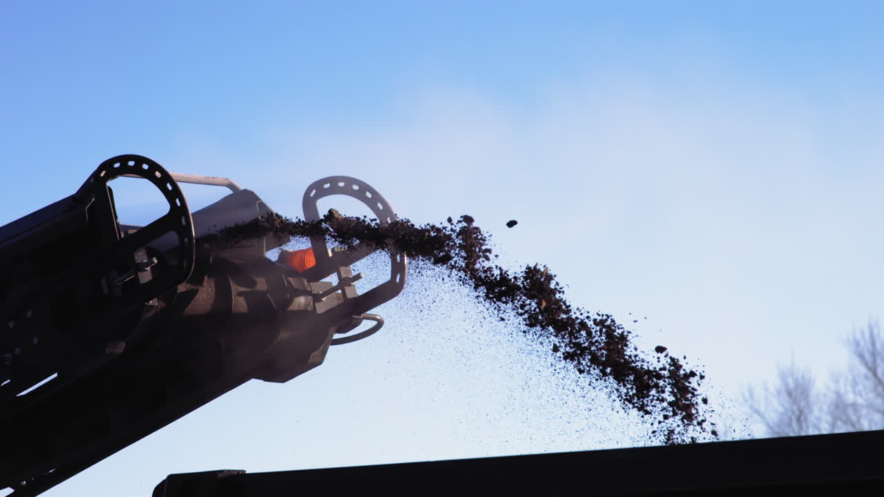 대형 건설 기계의 벨트에서 트럭으로 날아가는 땅 위 아스팔트의 느린 동작 영상