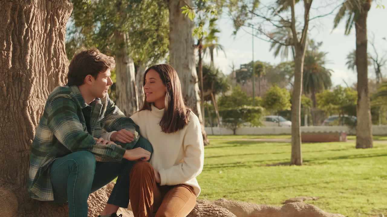Happy young young pair man and woman talking and laughing sitting in the park under