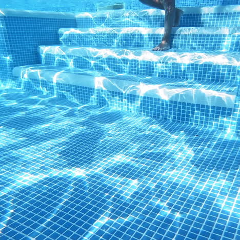 transparent underwater background in the swimming pool. underwater view of a boy's body coming down into the pool on stairs and swimming in blue clear water.