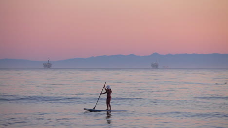 un paddle boarder filas a través del océano al atardecer 2