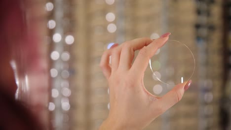 finger holds transparent contact lenses fashion accessory in hand. the womans delicate gesture held the transparent contact lenses between her thumb and finger, showcasing the intricate patterns on the glass fashion accessory