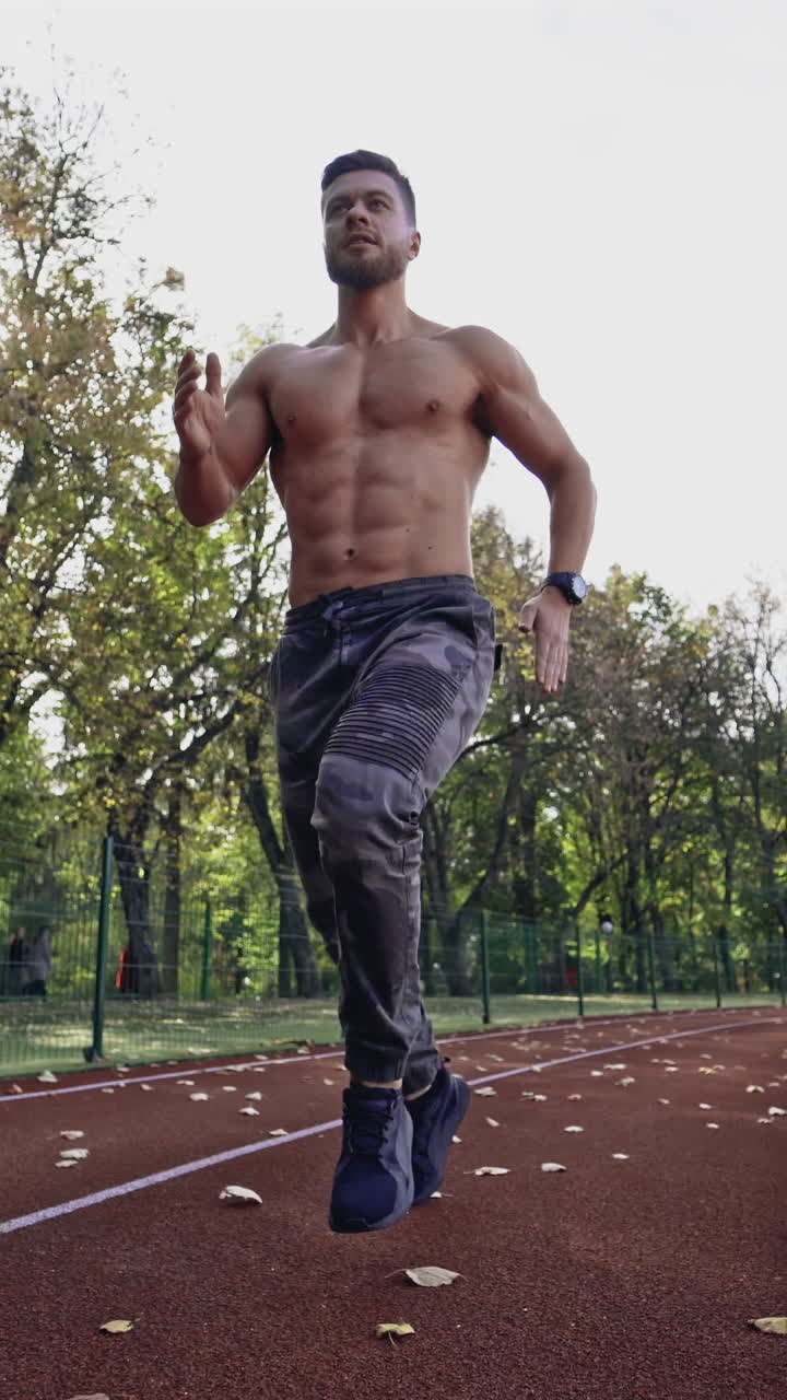 Handsome man training on the field stadium. Young muscular athlete runs on the sports track outdoors. Healthy lifestyle. Vertical video