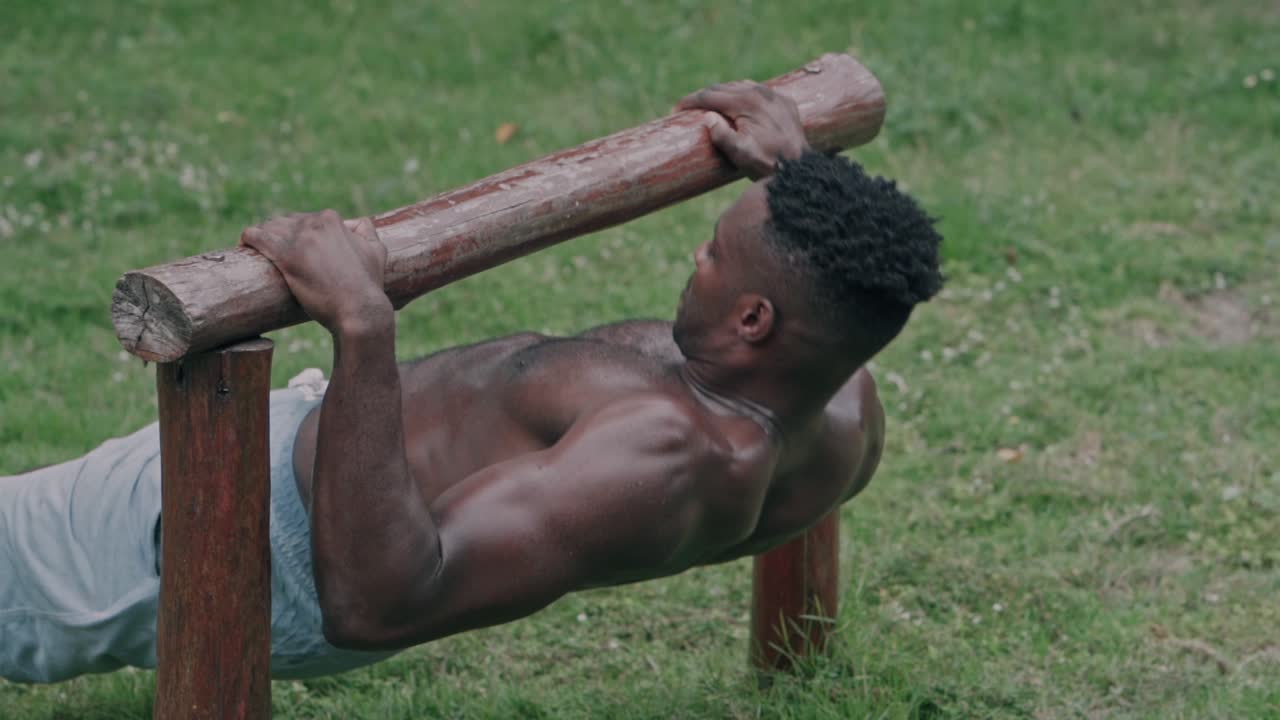 Muskulöser schwarzer Mann beim Inverted Row Training an Holzstange im Freien