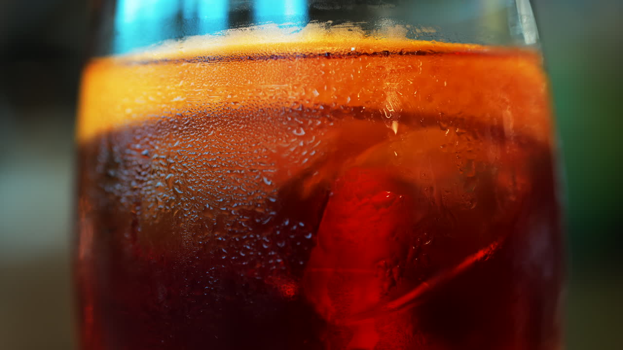 Close up of a Negroni cocktail with orange slice and ice cubes on a wooden table