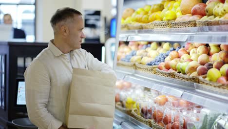 Ein-Erschossener-Besucher-Mittleren-Alters-Wählt-Äpfel-Aus-Einer-Vitrine-Aus-Und-Steckt-Sie-In-Eine-Papiertüte.-Umweltfreundliche-Verpackung.-Täglich