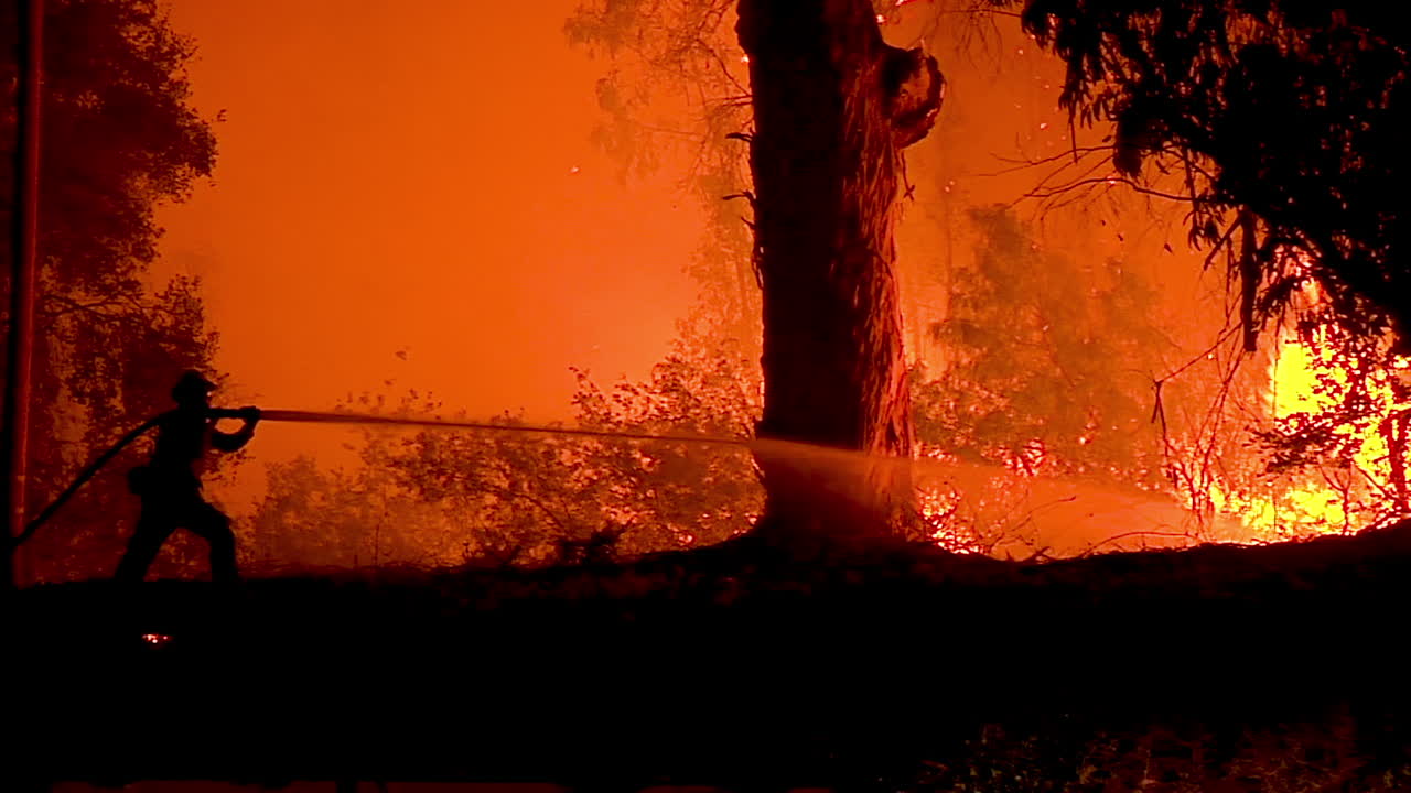 소방관은 실루엣으로 서서 휴일 화재 1 동안 거대한 산비탈 화재와 싸웁니다.