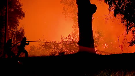 a firefighter stands in silhouette and fights a huge hillside blaze during the holiday fire 1