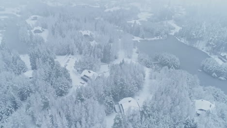 Aerial-tilt-up-shot-of-snowy-winter-landscape-with-house-and-frozen-lake-during-cold-winter